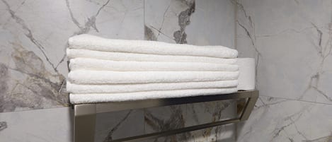 A bathroom with marble walls and a towel rack holding folded towels.