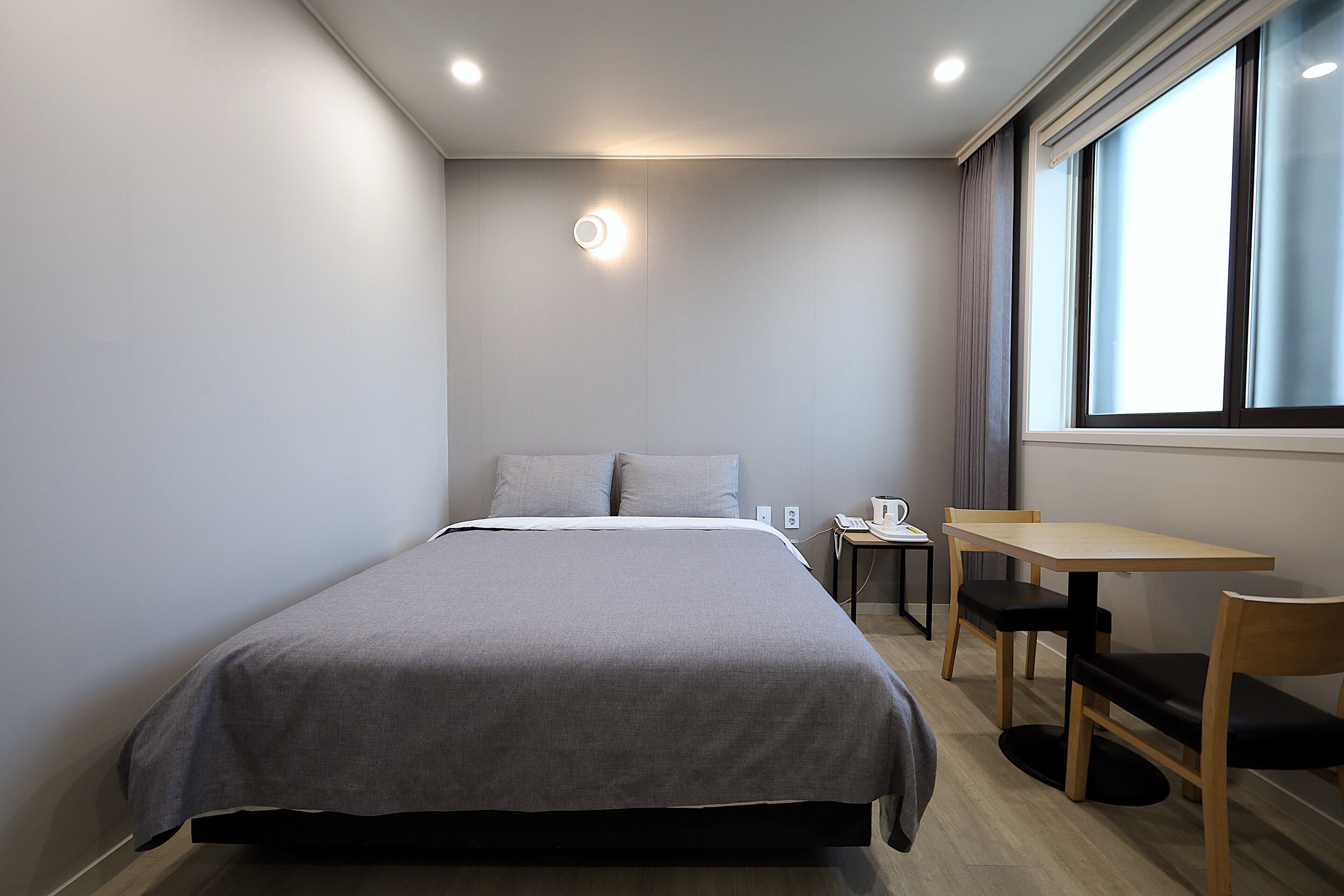 A modern hotel room with a bed, a small table, a chair, and a window with curtains.