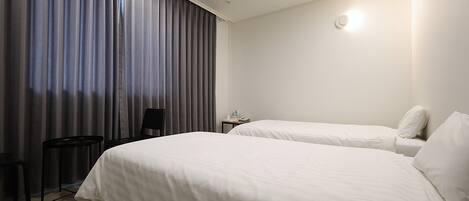 A hotel room with two beds, a small table, a chair, and a window with curtains.