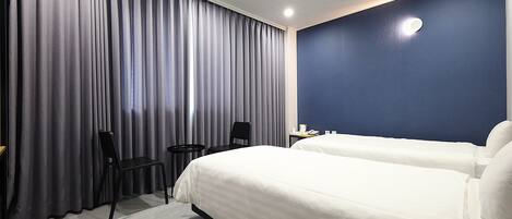 A hotel room with a large bed, two chairs, a small table, and a dark blue accent wall.