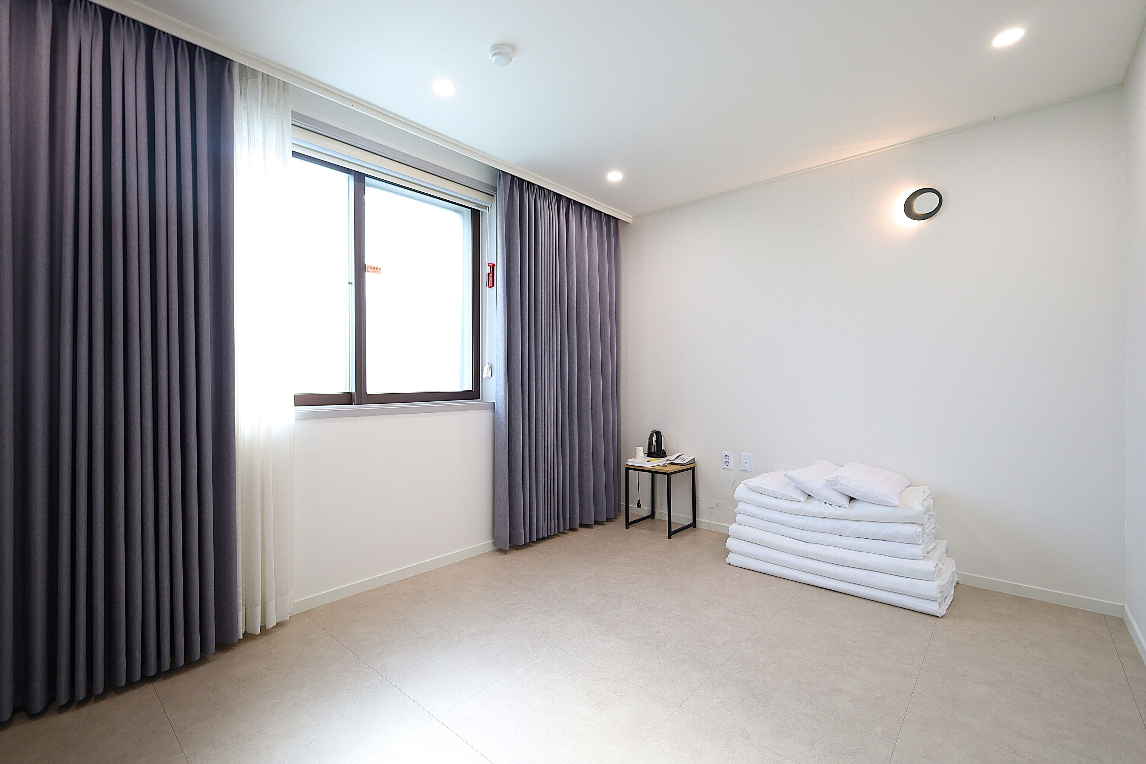 A hotel room with a large window, a small table with a kettle, and a stack of white towels.