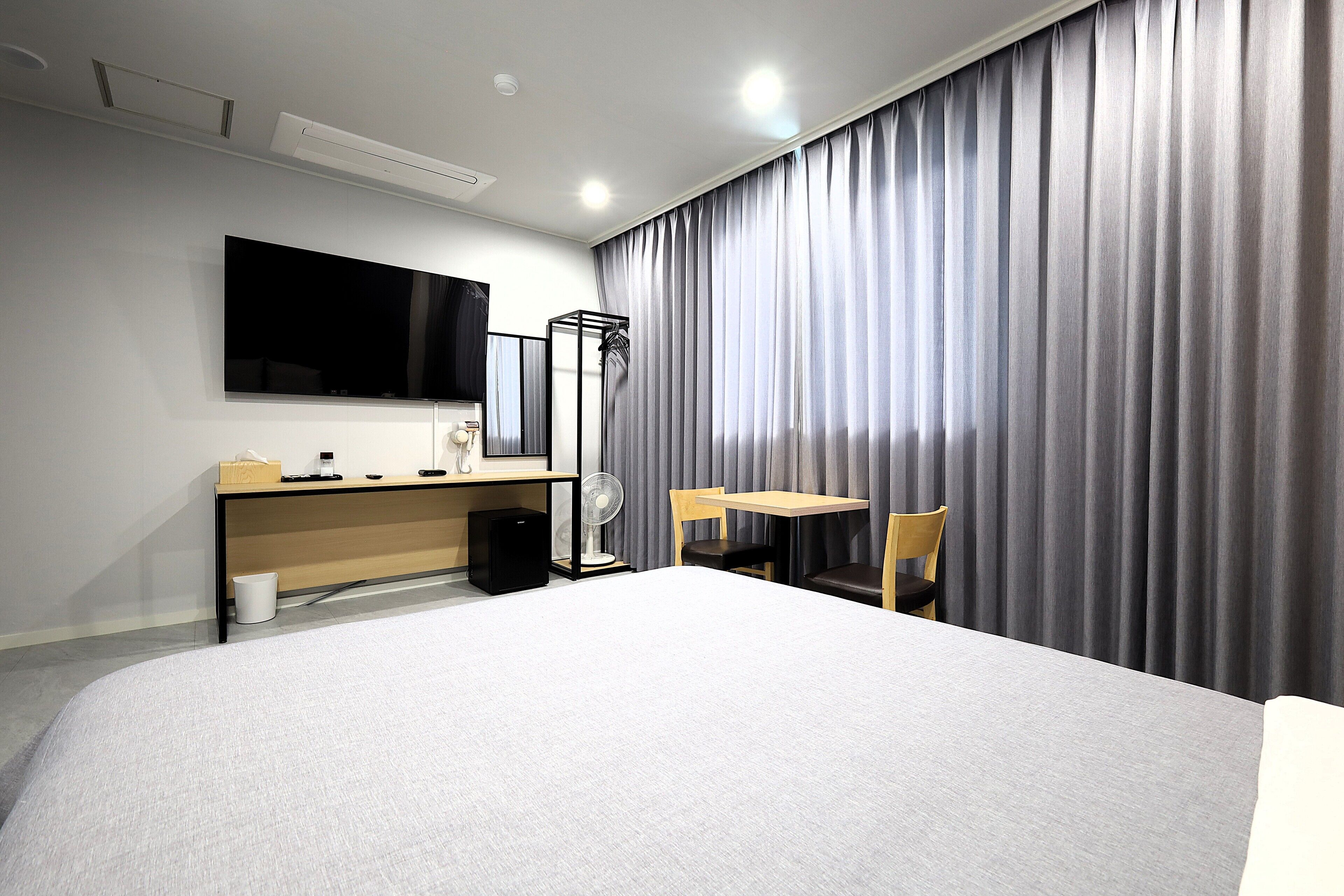 Une chambre d’hôtel avec un grand lit, un bureau avec un ordinateur, une chaise, un téléviseur fixé au mur et une fenêtre recouverte de rideaux.
