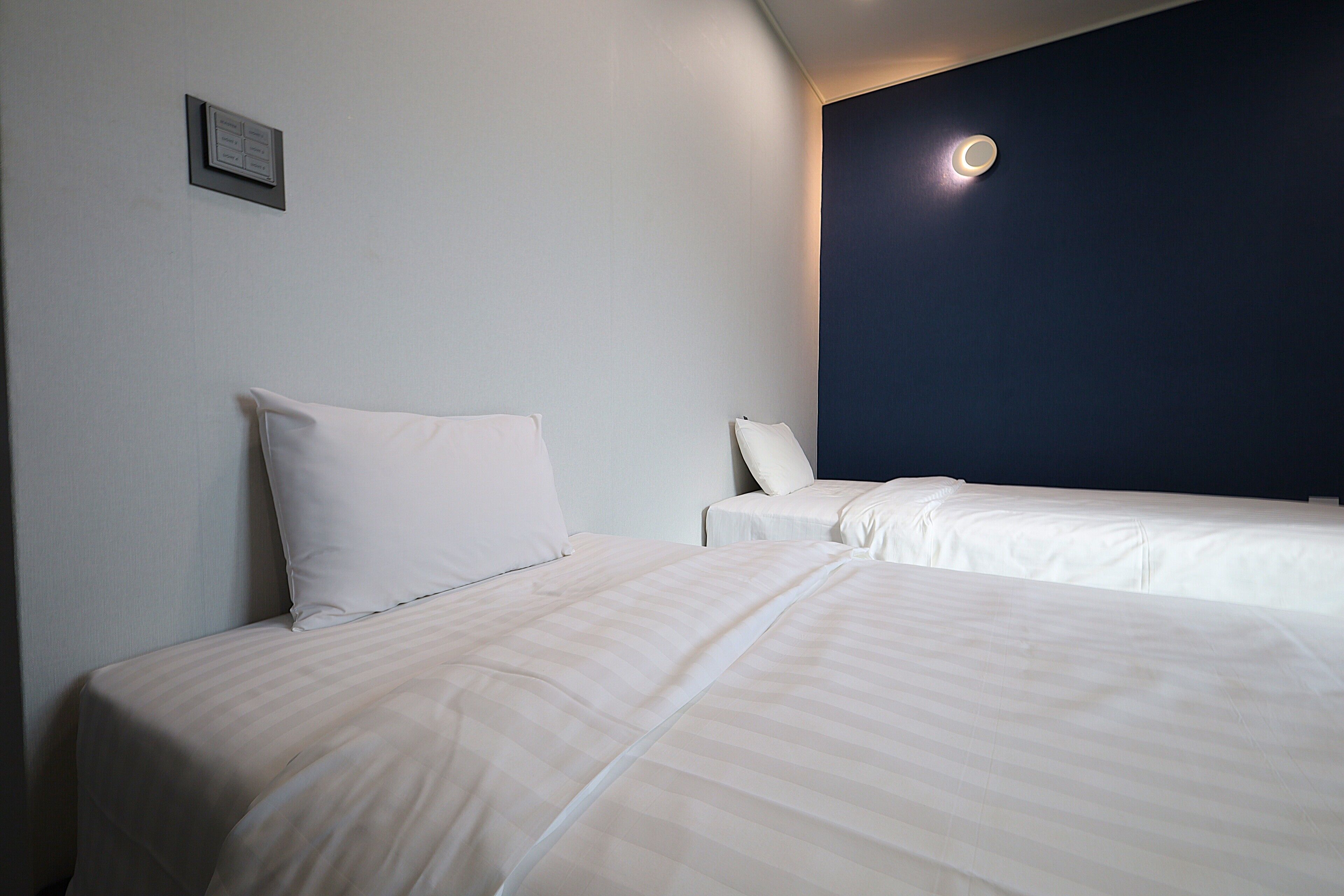 A hotel room with two beds, a dark accent wall, and a ceiling light fixture.
