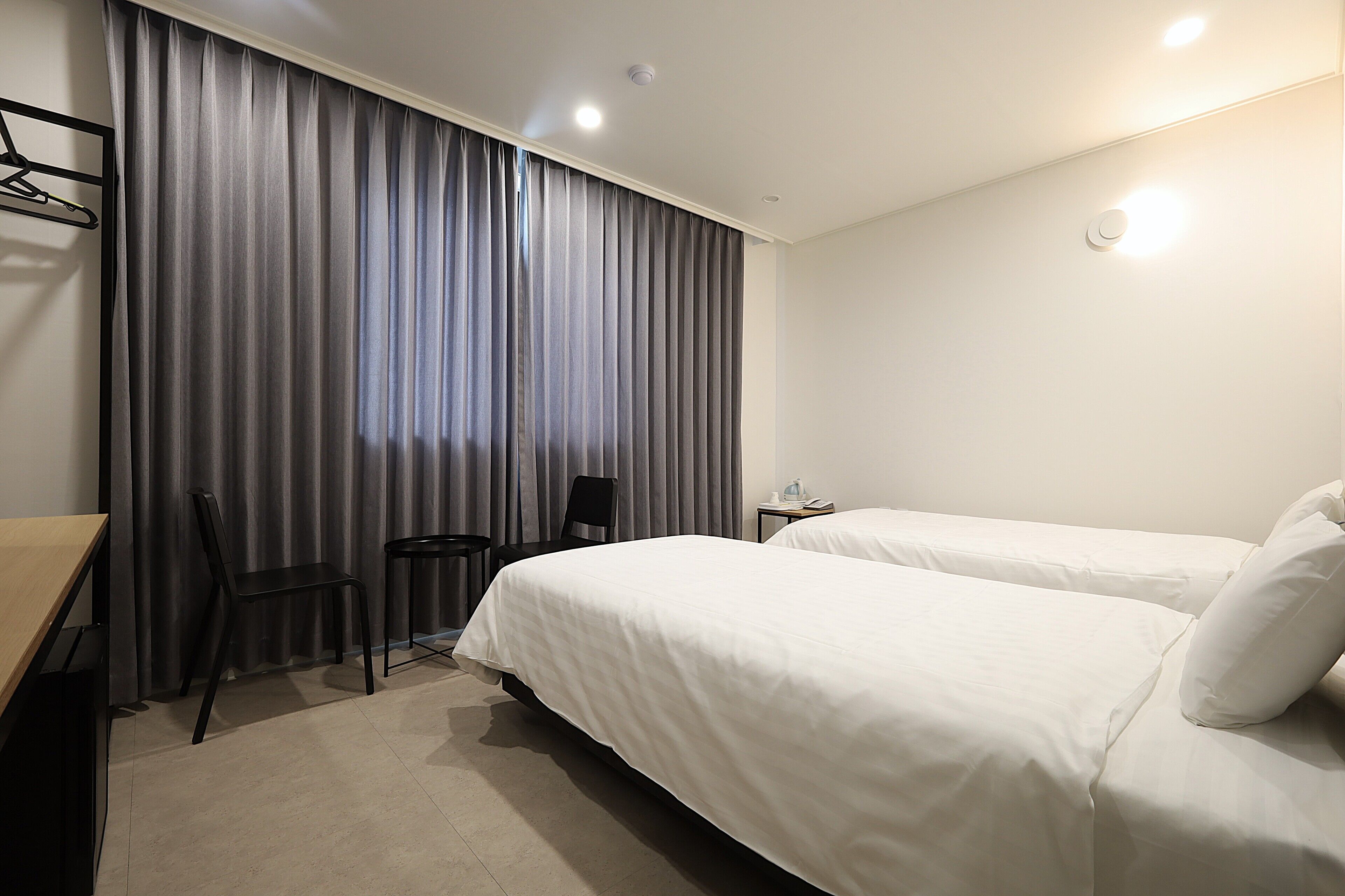 Une chambre d’hôtel avec deux lits, un bureau, une chaise et une fenêtre avec des rideaux.
