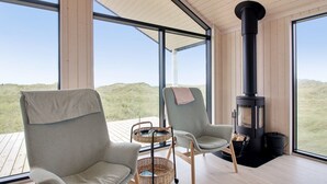 Quarto moderno com duas cadeiras, lareira e grandes janelas com vista para uma paisagem gramada.