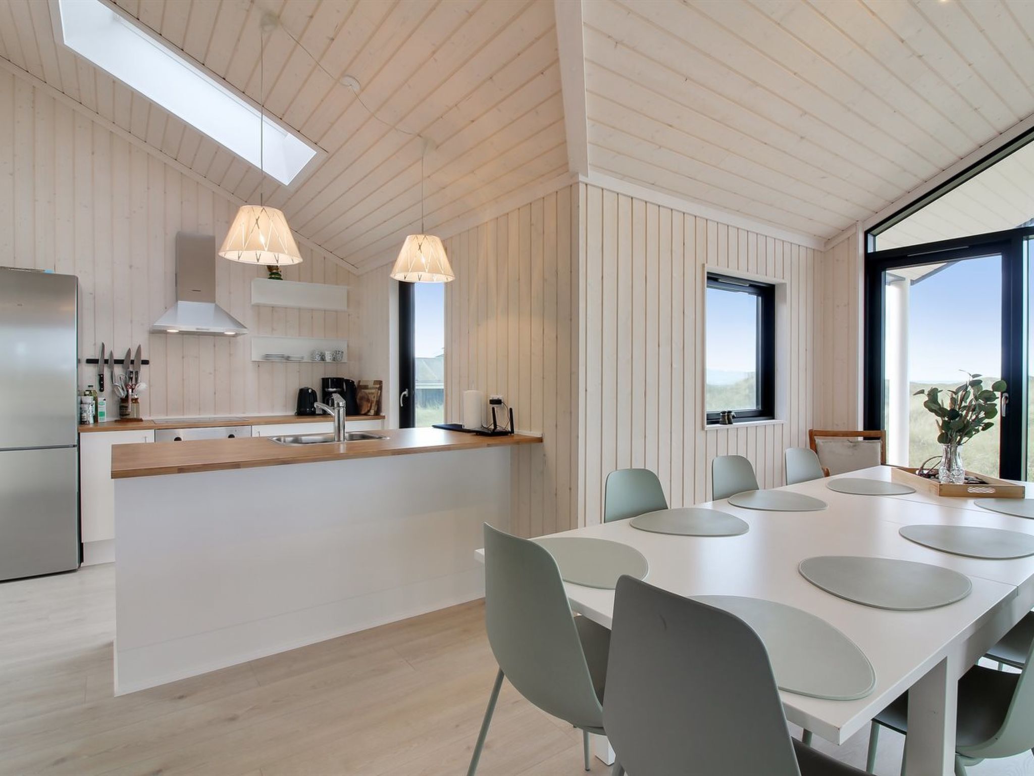 Une cuisine moderne dotée d’un îlot central, de luminaires suspendus et d’un coin repas avec une grande table et des chaises.