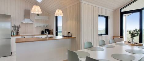 Une cuisine moderne dotée d’un îlot central, de luminaires suspendus et d’un coin repas avec une grande table et des chaises.