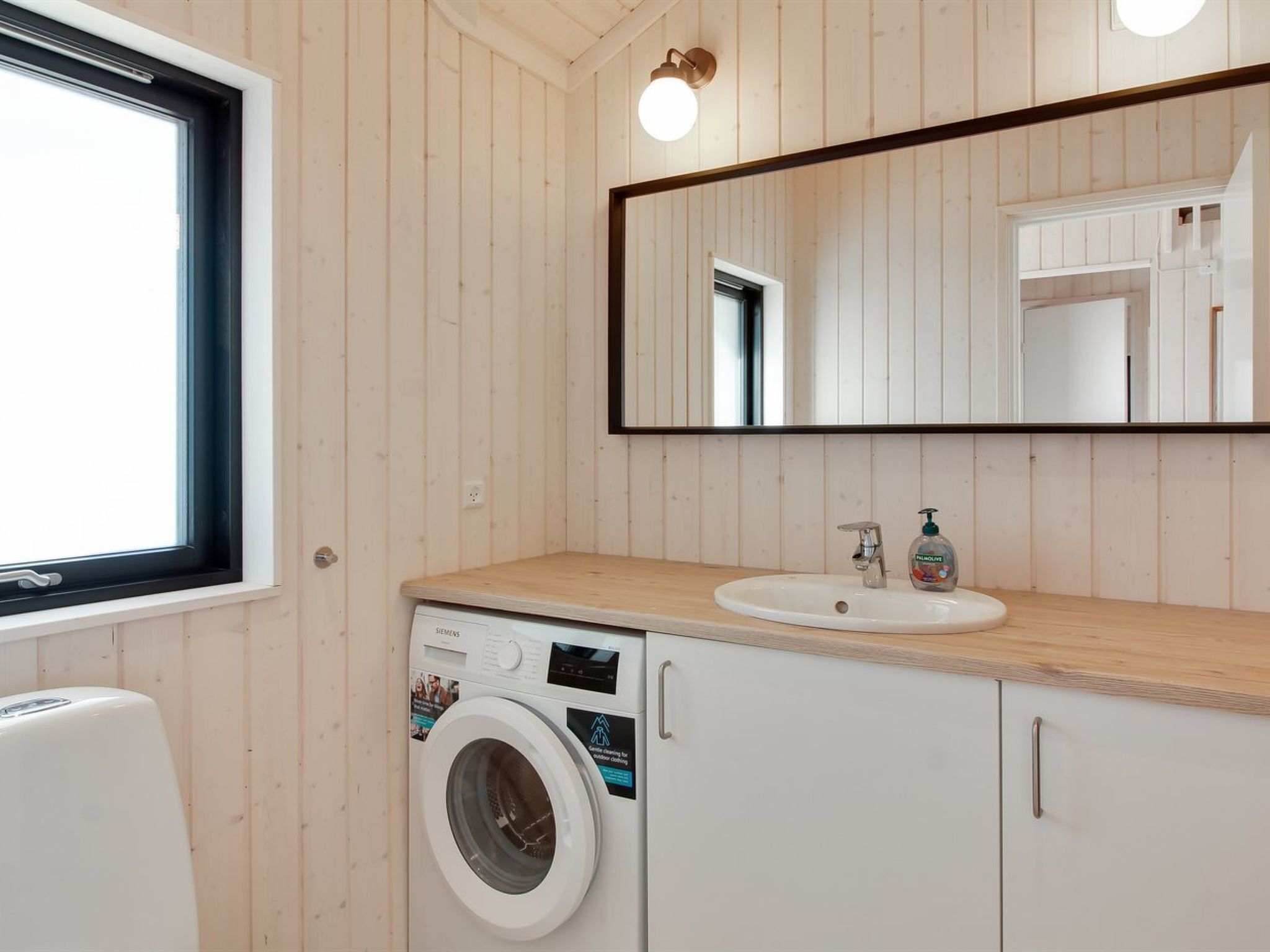 Ein kleines Badezimmer mit Waschmaschine, Waschbecken und Spiegel.