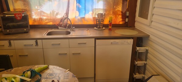 Una cocina con tostadora, lavamanos y ventana con vista a palmeras.