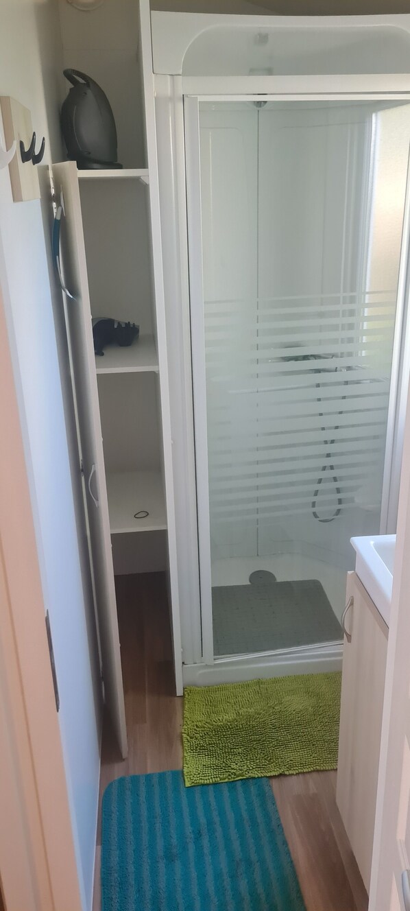 Un baño pequeño con cabina de ducha, una alfombra verde y un lavabo blanco.