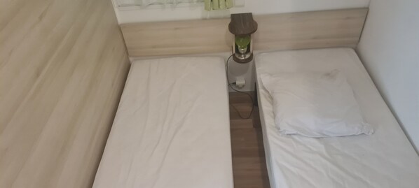 Una habitación pequeña con cama individual, cabecera de madera, lámpara de noche y almohada blanca.