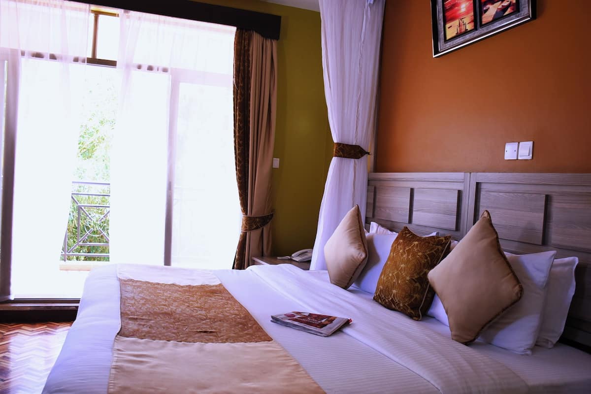 Habitación de hotel con una cama grande, un cabecero de madera y vistas a zonas verdes por la ventana.