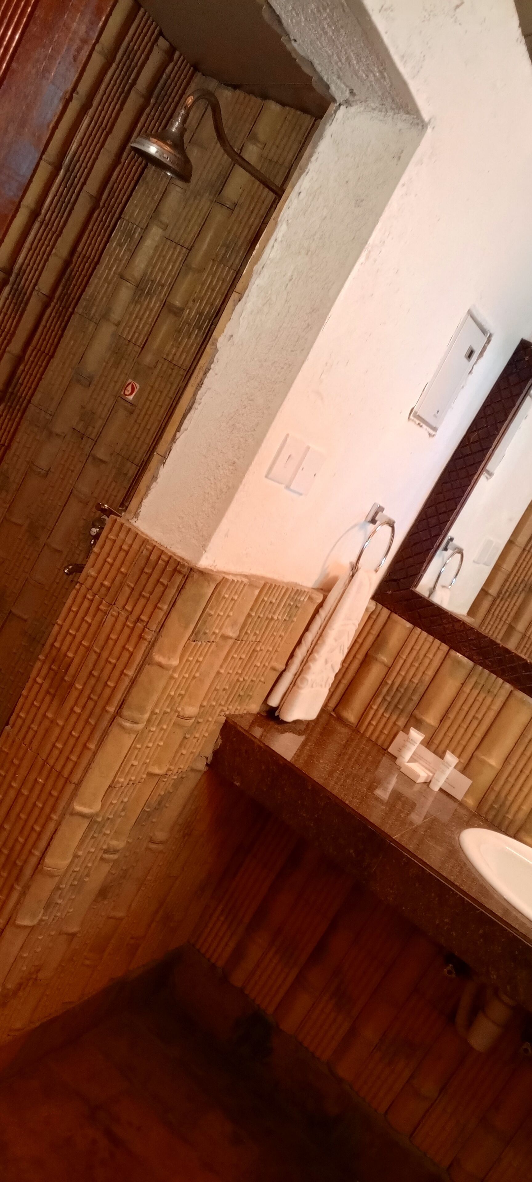 A bathroom with a wooden floor, a shower with a handheld showerhead, a sink with a mirror, and a towel hanging on the wall.
