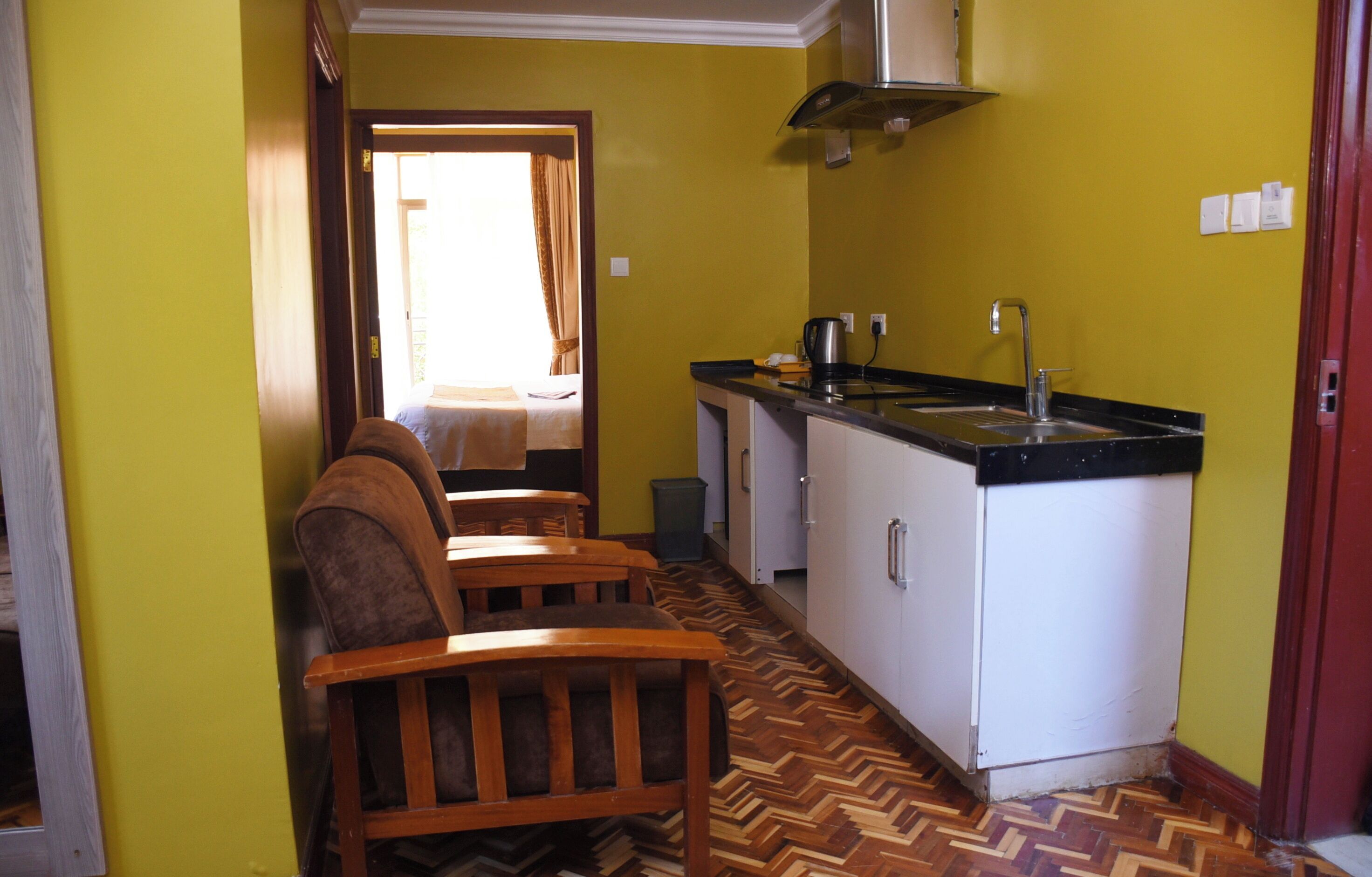 A compact kitchen with a herringbone-patterned floor, wooden chairs, and a small dining table.