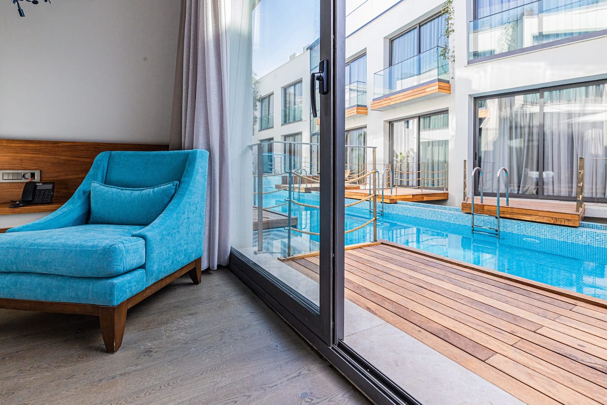 Una habitación de hotel moderna con un ventanal grande, un sofá azul y vistas a una piscina.