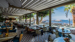An outdoor café with tables and chairs, a checkered floor, and a view of the sea. - Gözegir Hotel - Adults Only (Bodrum)