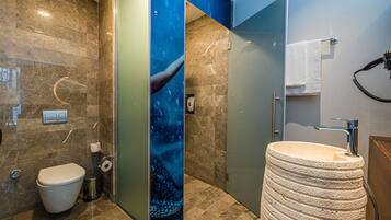 A bathroom with a marble wall, a white toilet, a sink with a stone basin, and a towel rack.