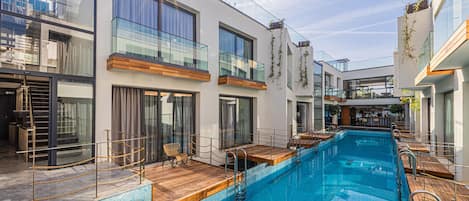Un hotel moderno con piscina, terraza de madera y barandillas de vidrio.