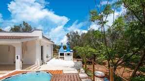 Un área de piscina con muelle de madera, un edificio blanco con tejado de baldosas y una chimenea azul.