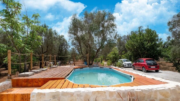 Una piscina con cubierta de madera, paredes de piedra y un coche aparcado cerca.