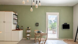 Una cocina con un armario blanco, una mesa de madera y una silla. Hay una estantería con botellas y un marco de fotos.