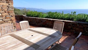 A wooden table and chairs set on a patio with a stone wall and a view of the ocean. - Villa in Gaou with Sea View and Beach (Bormes-les-Mimosas)