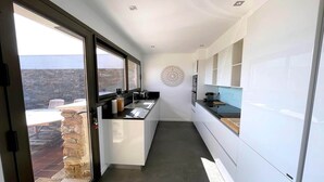 A modern kitchen with a stone wall, a large window, and a decorative wall piece. - Villa in Gaou with Sea View and Beach (Bormes-les-Mimosas)