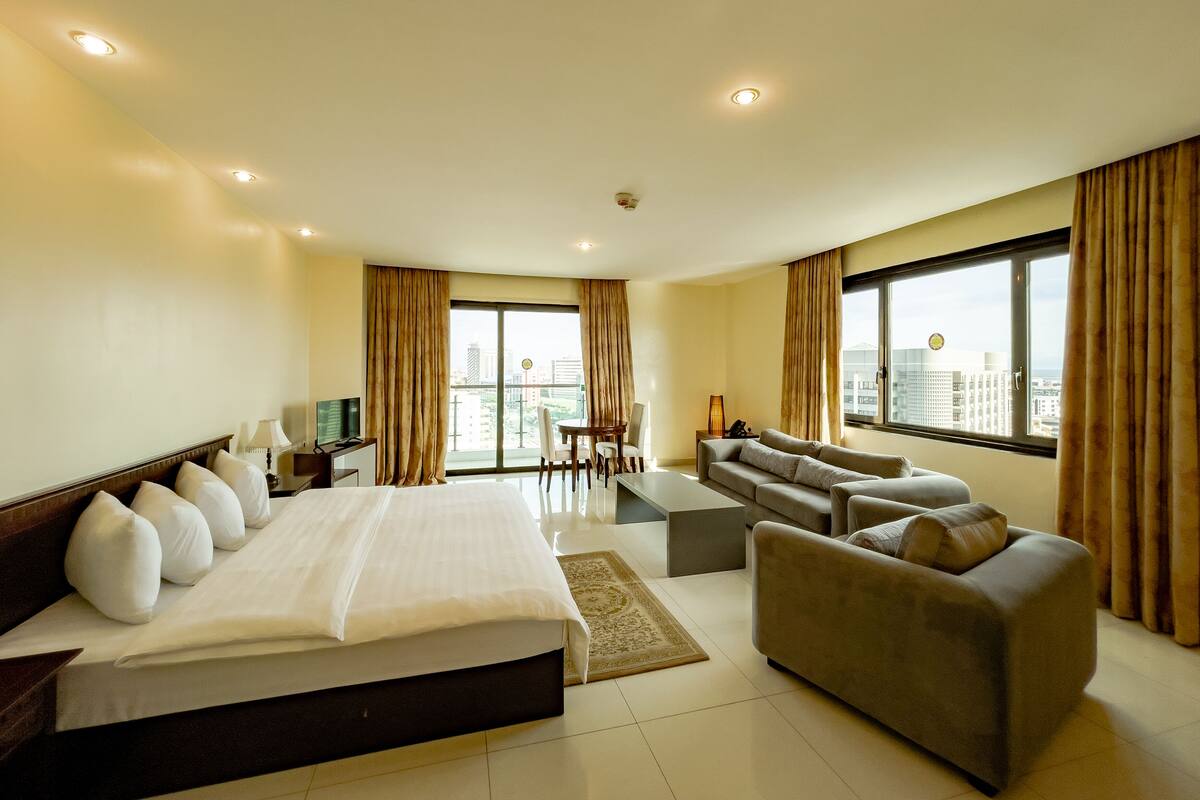 A hotel room with a large bed, a sofa, a desk, and a view of the city.