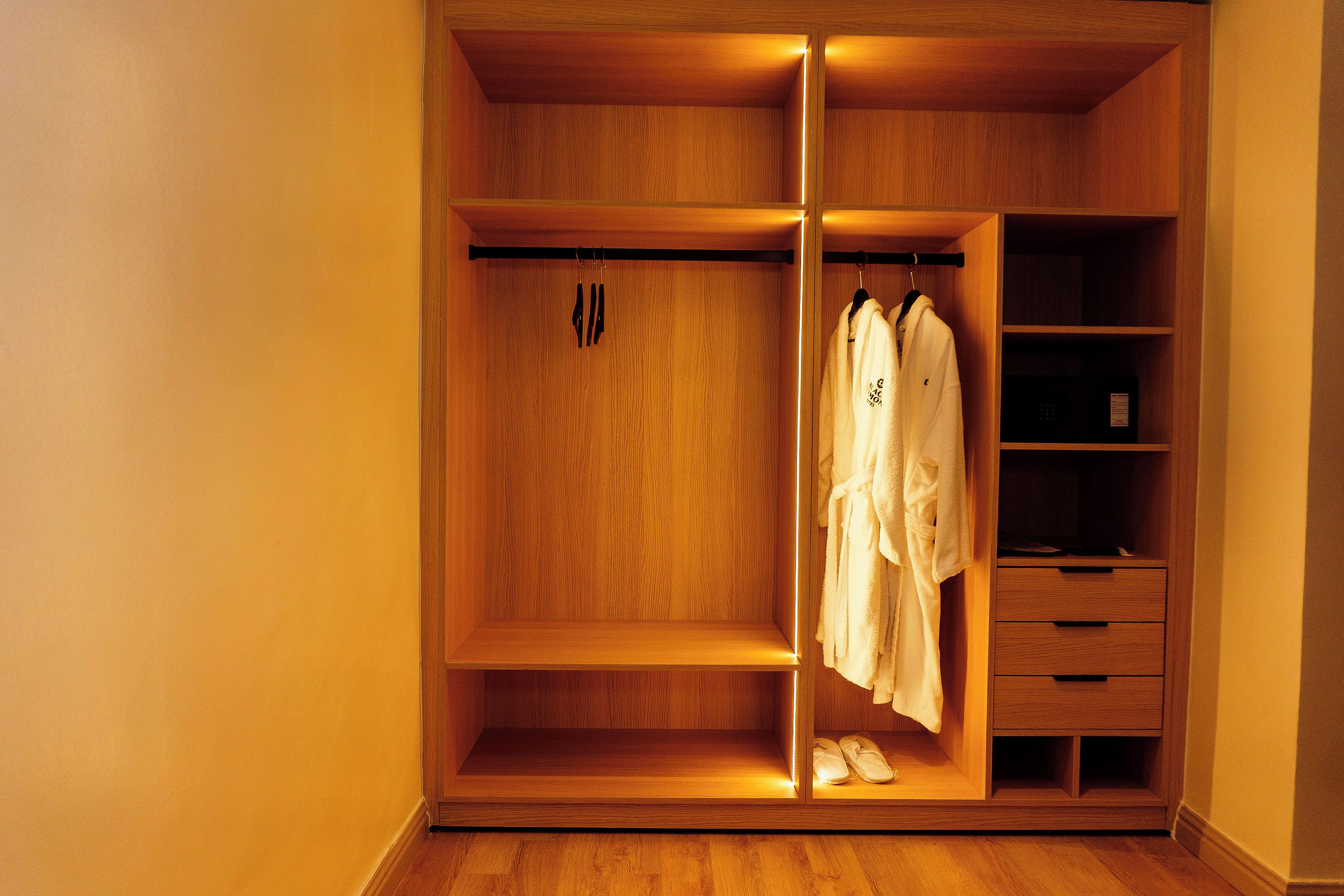 Un armario de madera con varios estantes y espacio para colgar ropa, un par de zapatos en el estante inferior y una bata colgada en el lado derecho.