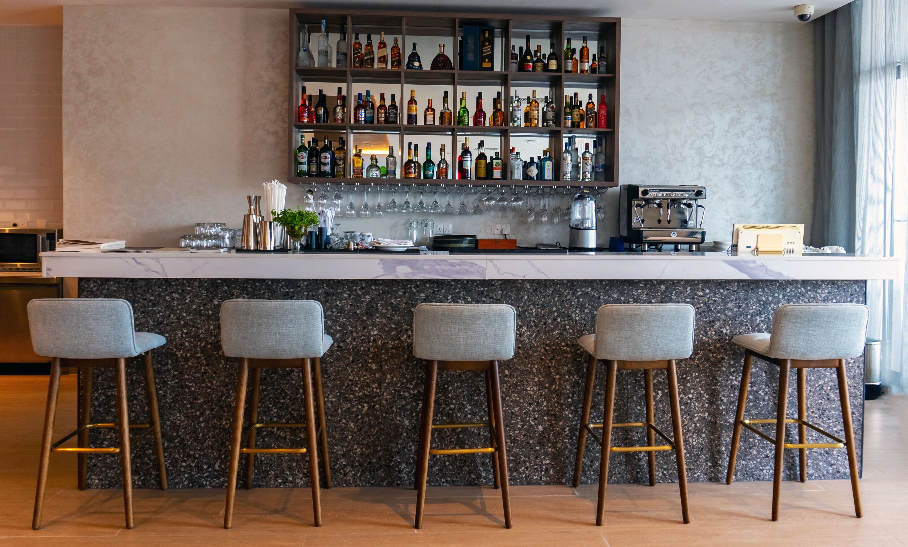 A bar area with a marble countertop, multiple stools, a coffee machine, and a variety of bottles.