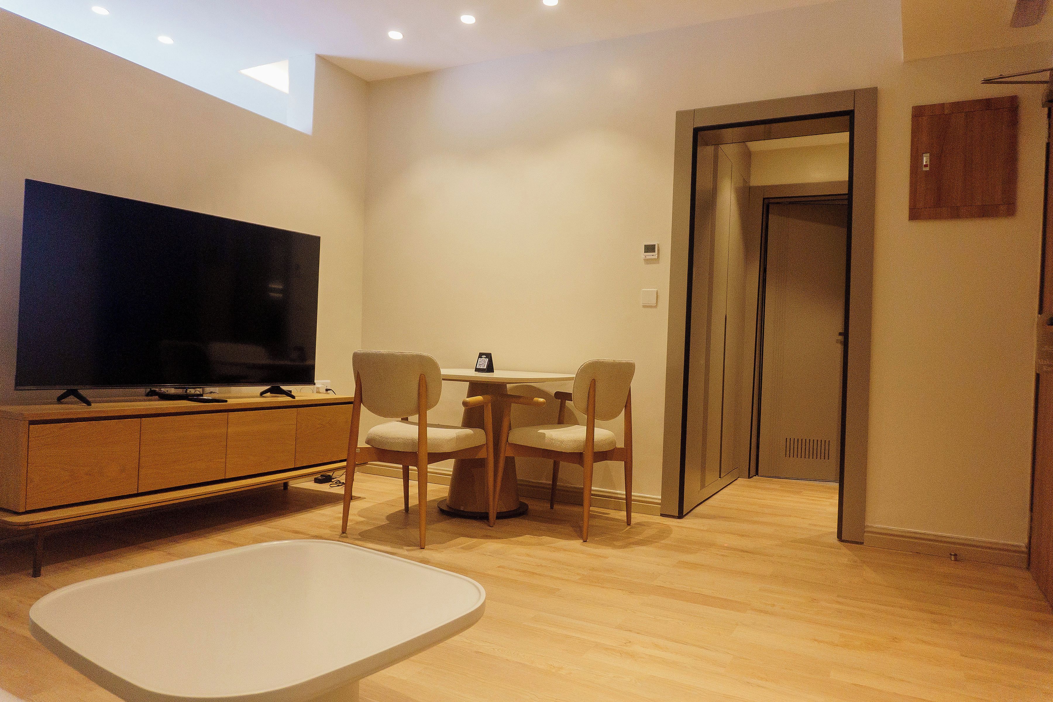 A modern living room with a flat-screen TV, wooden furniture, and a small table.