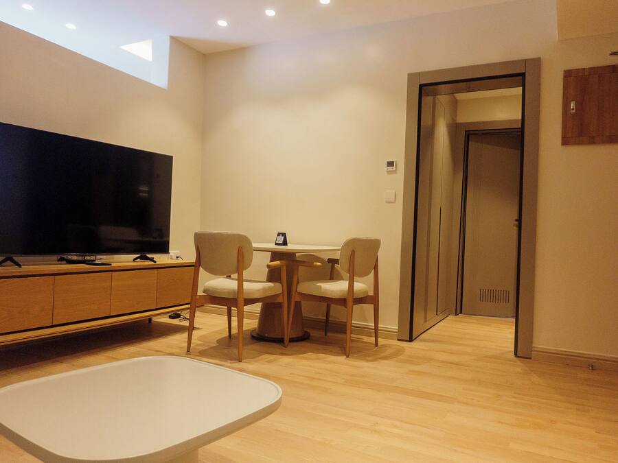 A modern living room with a flat-screen TV, wooden furniture, and a small table.