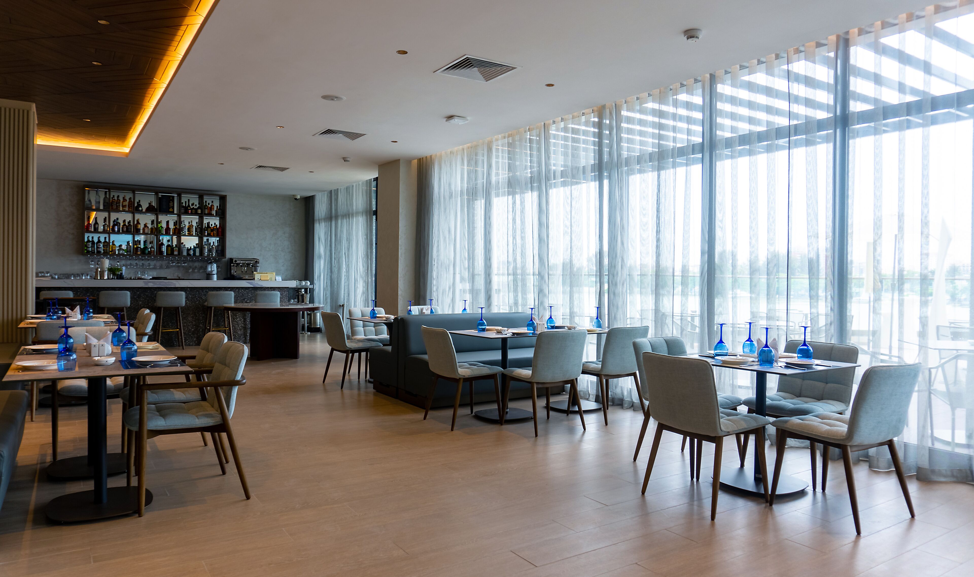 A modern restaurant with a bar area, large windows, and a variety of seating options.