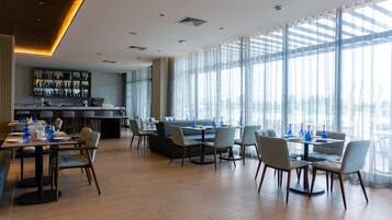 A modern restaurant with a bar area, large windows, and a variety of seating options.