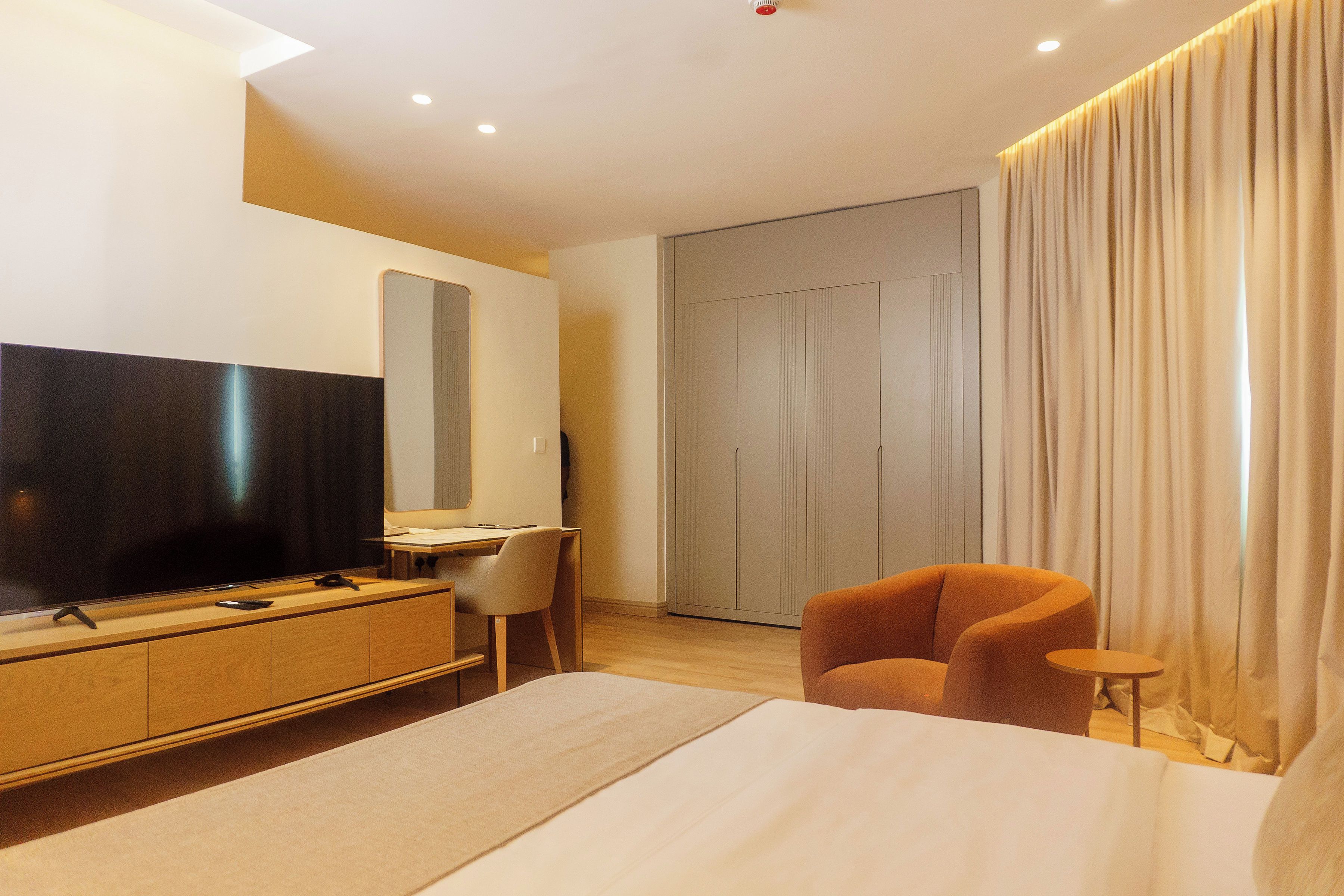 A modern hotel room with a large bed, a desk, a television, and a wardrobe.