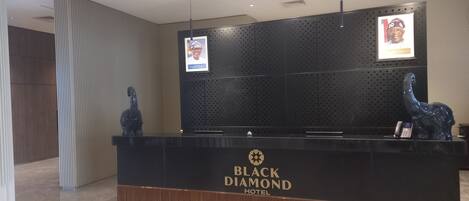 A reception desk at Black Diamond Hotel with a modern design, featuring a logo, a telephone, and a decorative sculpture.