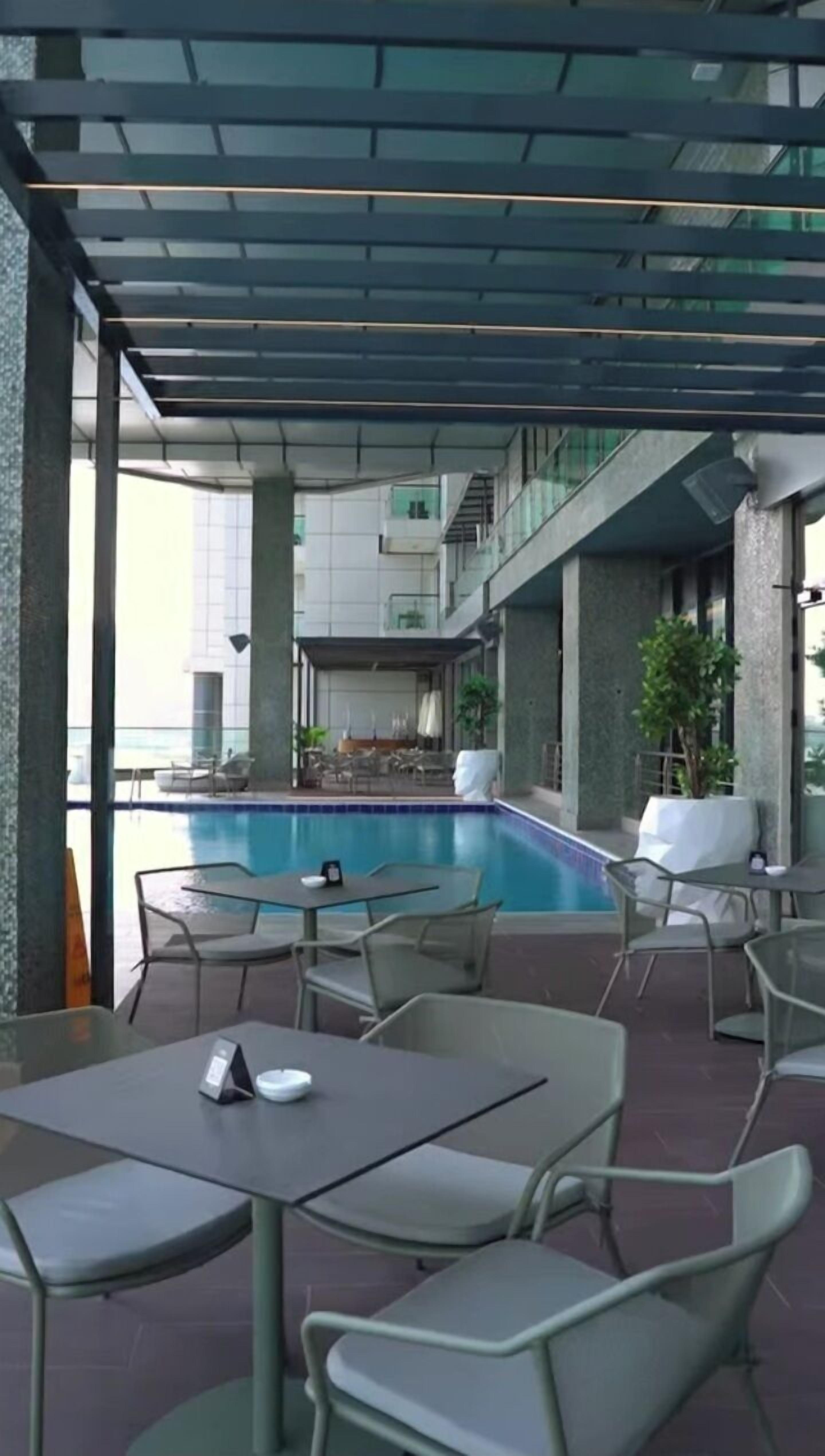 Un espace piscine extérieur doté de chaises longues et de tables, entouré d’une terrasse couverte offrant une vue sur la piscine.