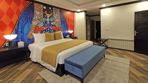 Een hotelkamer met een groot bed, een bankje, een nachtkastje met een lamp, een wandtapijt en een radiator.