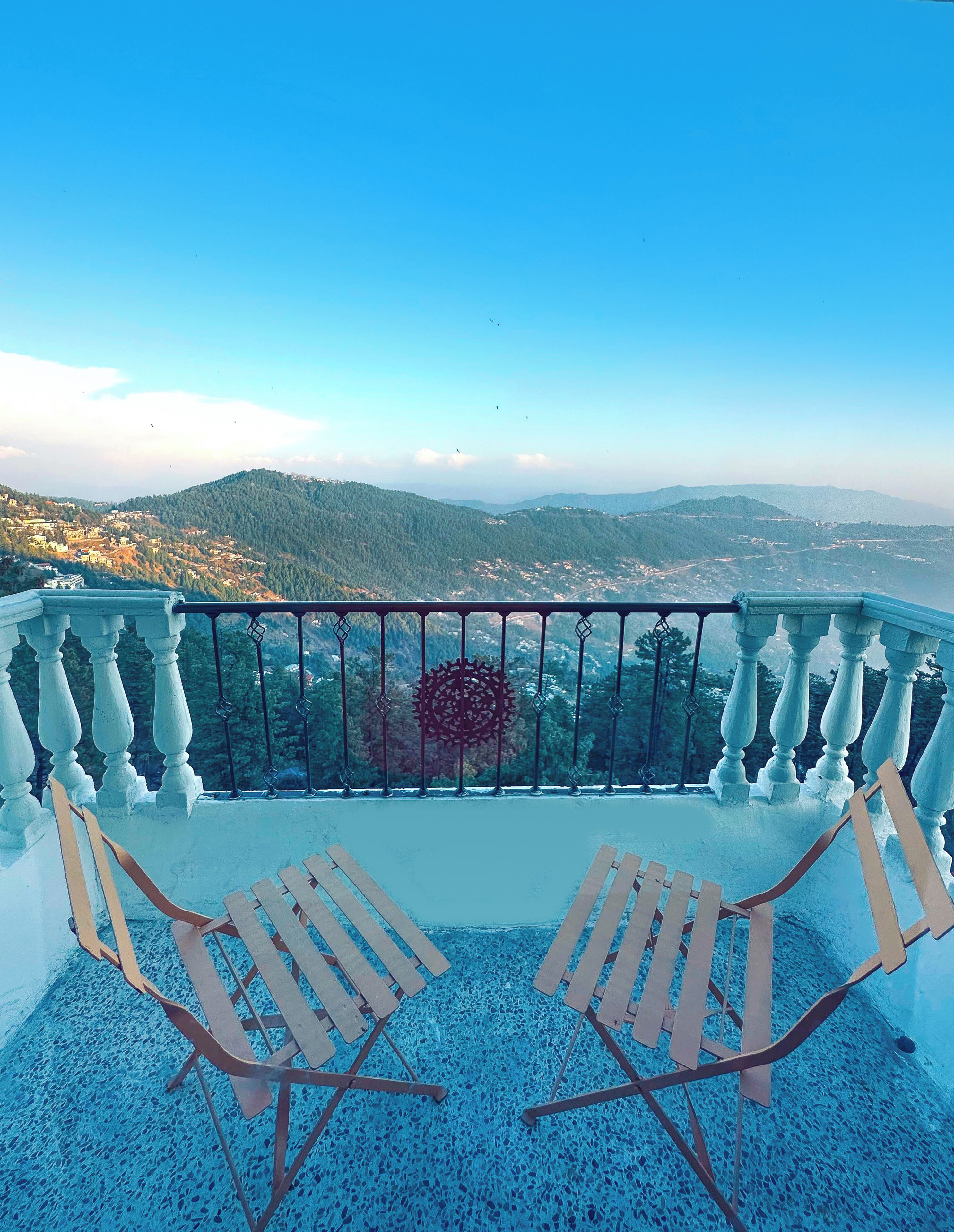 A balcony with two wooden chairs and a decorative metal railing overlooking a mountainous landscape.
