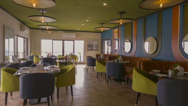 Een restaurant met ronde tafels en stoelen, grote ramen en een groen plafond.