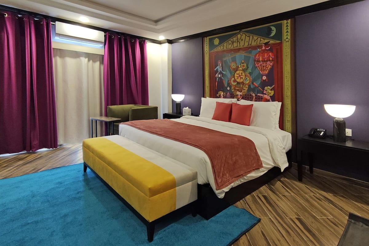 A hotel room with a large bed, a desk, a chair, and a window with curtains.