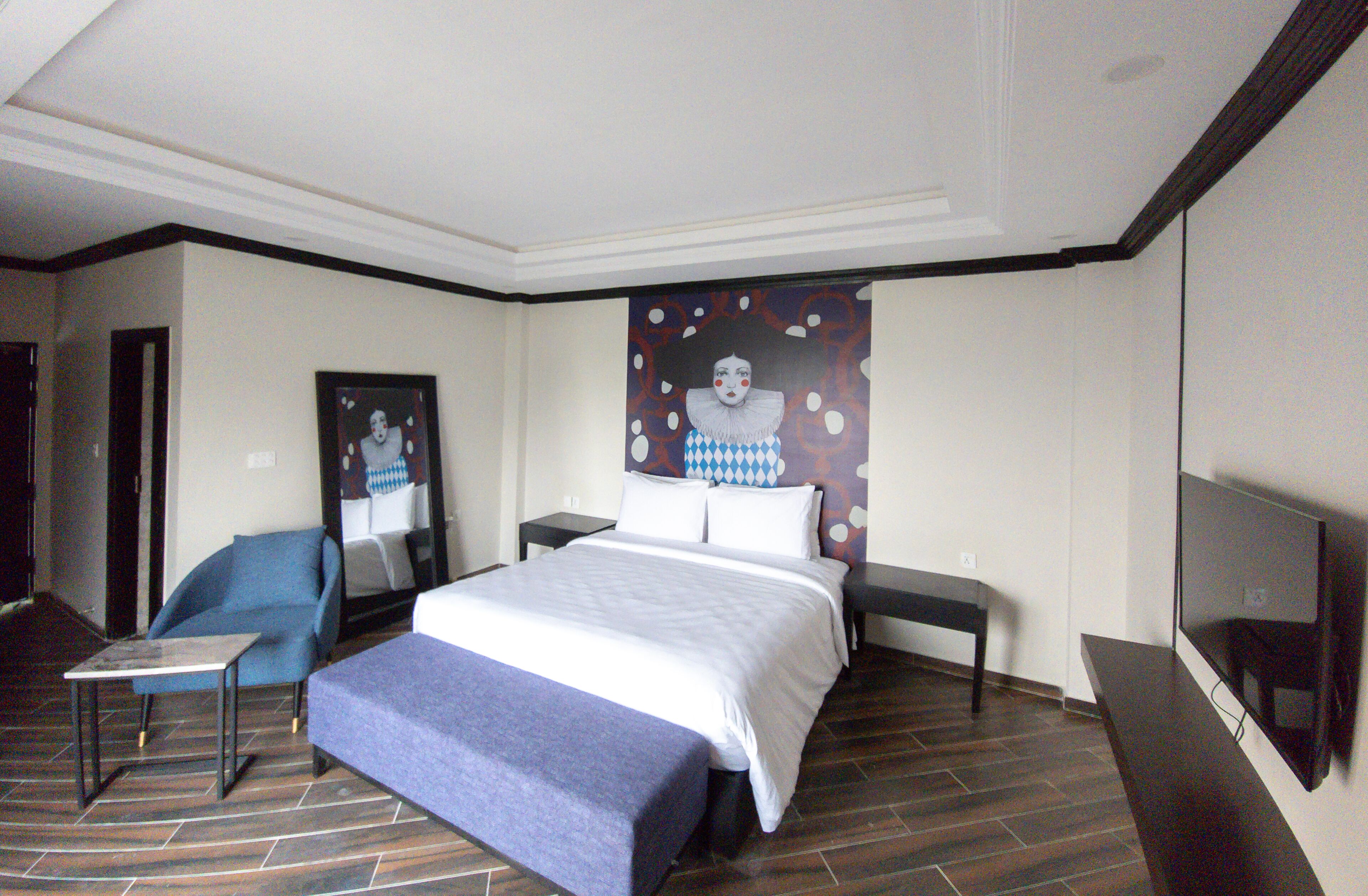 A hotel room with a bed, a chair, a TV, and a painting on the wall.