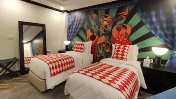 Une chambre d’hôtel avec deux lits, chacun recouvert d’une couvre-lit à carreaux rouges et blancs, un grand miroir et une fresque colorée sur le mur.
