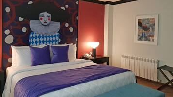 A hotel room with a bed, a nightstand, a lamp, a radiator, and a large abstract painting on the wall.