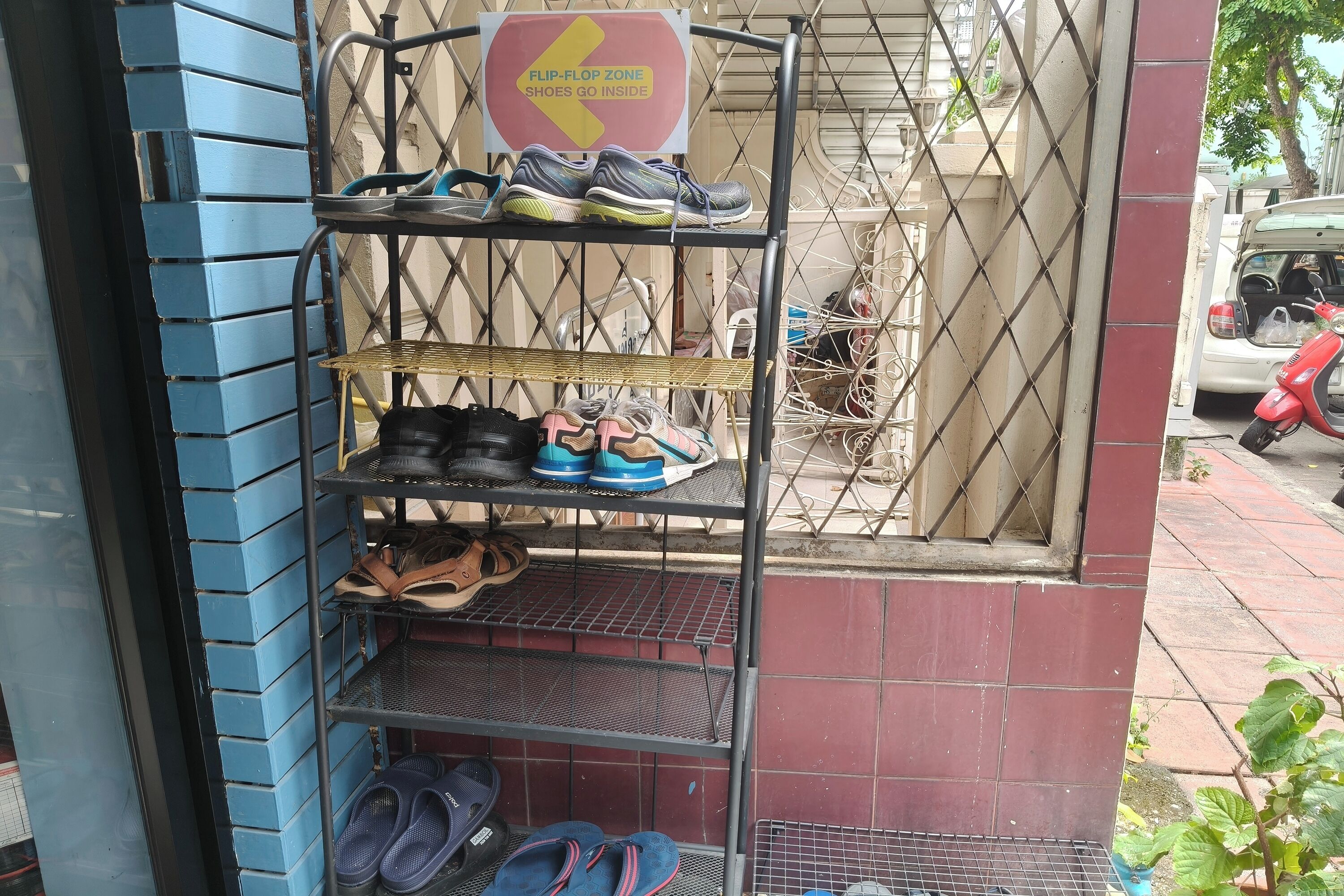 A metal rack with various pairs of shoes and flip-flops, a sign indicating a flip-flop zone, and a scooter parked outside.
