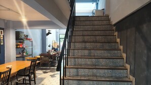 A staircase with patterned tiles leading to an upper floor, a wooden dining table with chairs, and a shelf with various items. - El biografo hostel (Bangkok)
