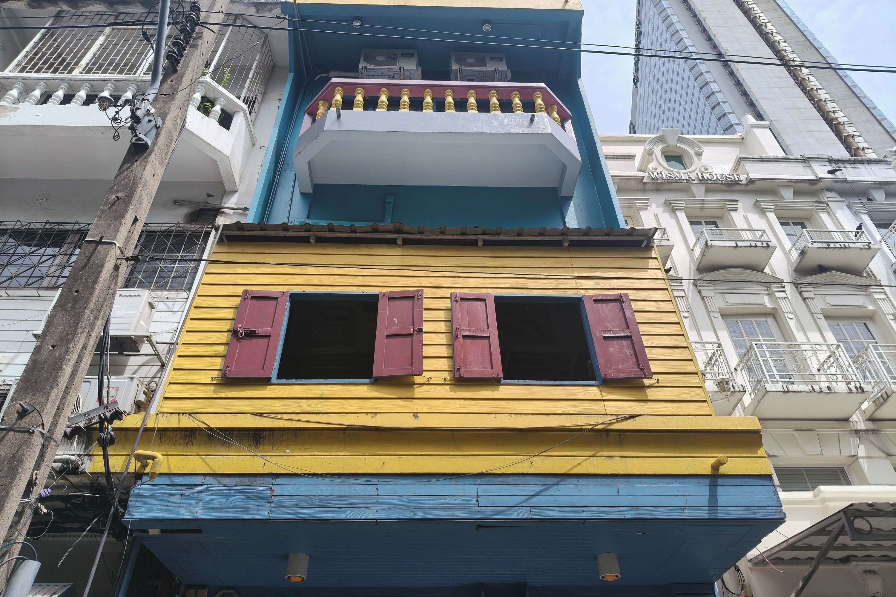 A multi-story building with balconies, a visible air conditioning unit, and a sign reading "MISTA HOUSE".
