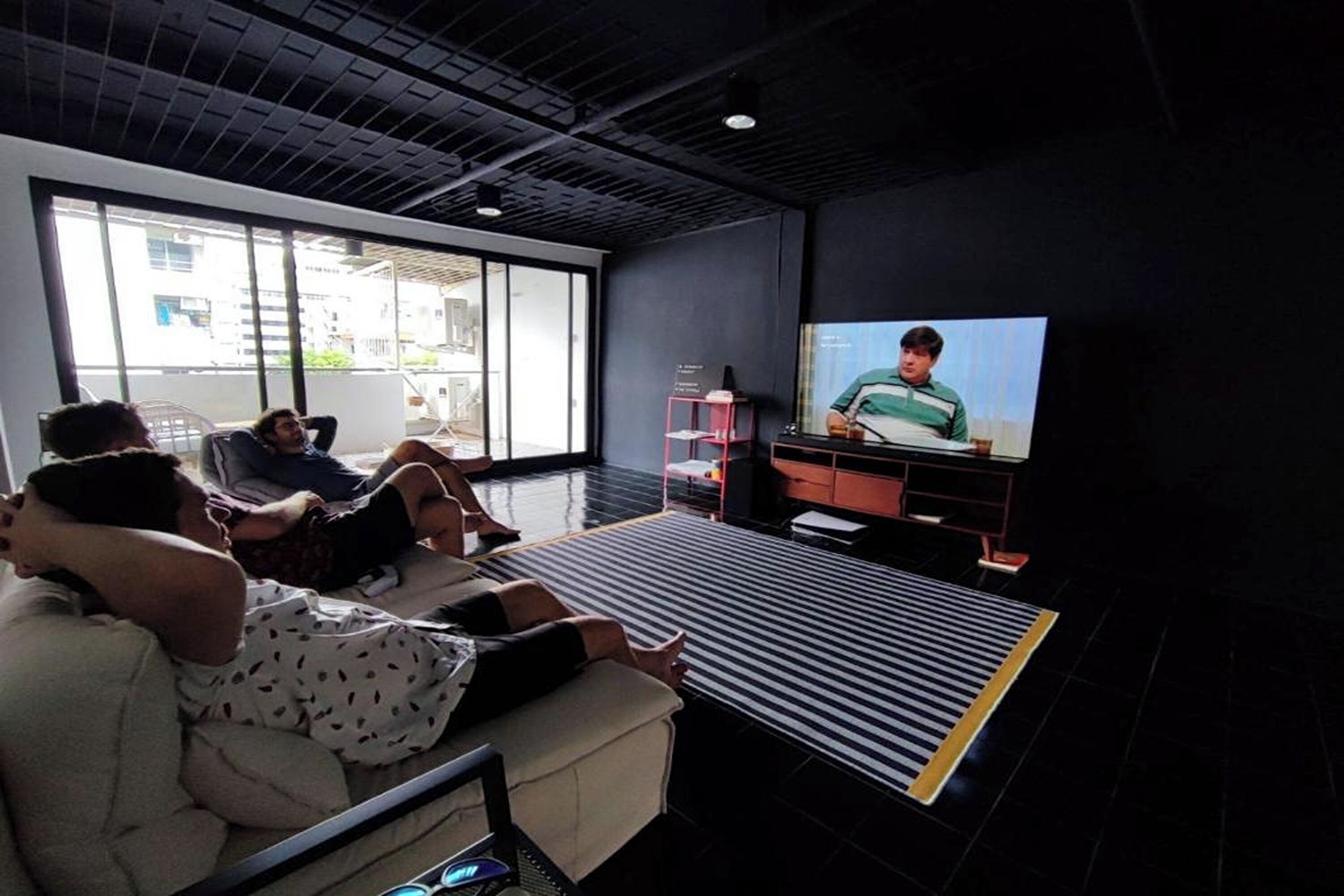 A modern living room with a large flat-screen TV, comfortable seating, and a large window offering a view of the outside.