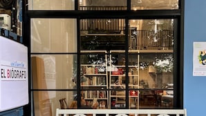 A room with a large window, a white bench, and a bookshelf filled with books. - El biografo hostel (Bangkok)