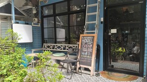 A hostel with a signboard indicating it's open, outdoor seating, and a view through the window. - El biografo hostel (Bangkok)